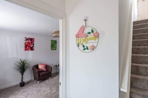 A hallway with a welcome sign, a brown leather chair, a potted plant, and a staircase.