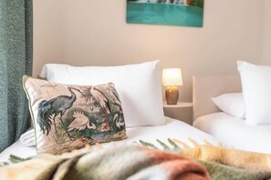 A hotel room with a bed, white pillows, a nightstand with a lamp, and a painting on the wall.