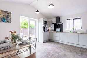 A modern kitchen with white cabinets, a black range hood, and a dining area with a table set for four. - Beverley Central Quiet 3 bedroom Homey Parking (East Riding of Yorkshire)