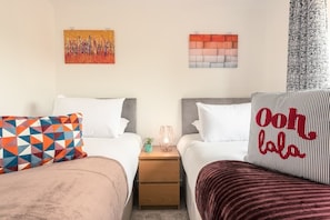 Ein Hotelzimmer mit zwei Betten, einem Nachttisch, einem kleinen Tisch mit Lampe und Kunstwerken an den Wänden.