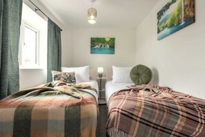 A room with two beds, a window with curtains, a wall-mounted picture, and a hanging light fixture.