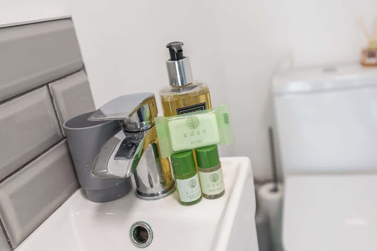 A bathroom sink with a soap dispenser, a bottle of liquid soap, and two bottles of body wash.