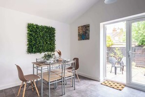 A dining area with a table, chairs, a green wall decoration, and a view through a glass door.