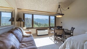 A room with a large window offering a mountain view, a leather sofa, a dining table with chairs, and a hanging light fixture. - Valley Vista Escape (Durango)