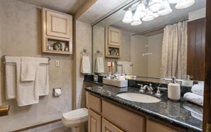 A bathroom with a sink, toilet, and mirror. There are towels hanging on the wall and a shelf with toiletries. - Valley Vista Escape (Durango)