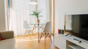 A modern living room with a glass dining table, two white chairs, a potted plant, a television, and a remote control on a stand. - Oporto Yellow Apartments104 (Porto)