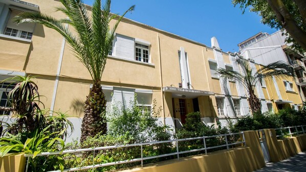 A yellow building with white window frames, a balcony, and a palm tree in the foreground.