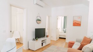 Un saló modern amb televisió de pantalla plana, una taula de menjar de vidre i un sofà amb coixins.