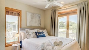 Une chambre à coucher avec un lit, un ventilateur de plafond, une fenêtre avec des rideaux et une vue sur l’extérieur.
