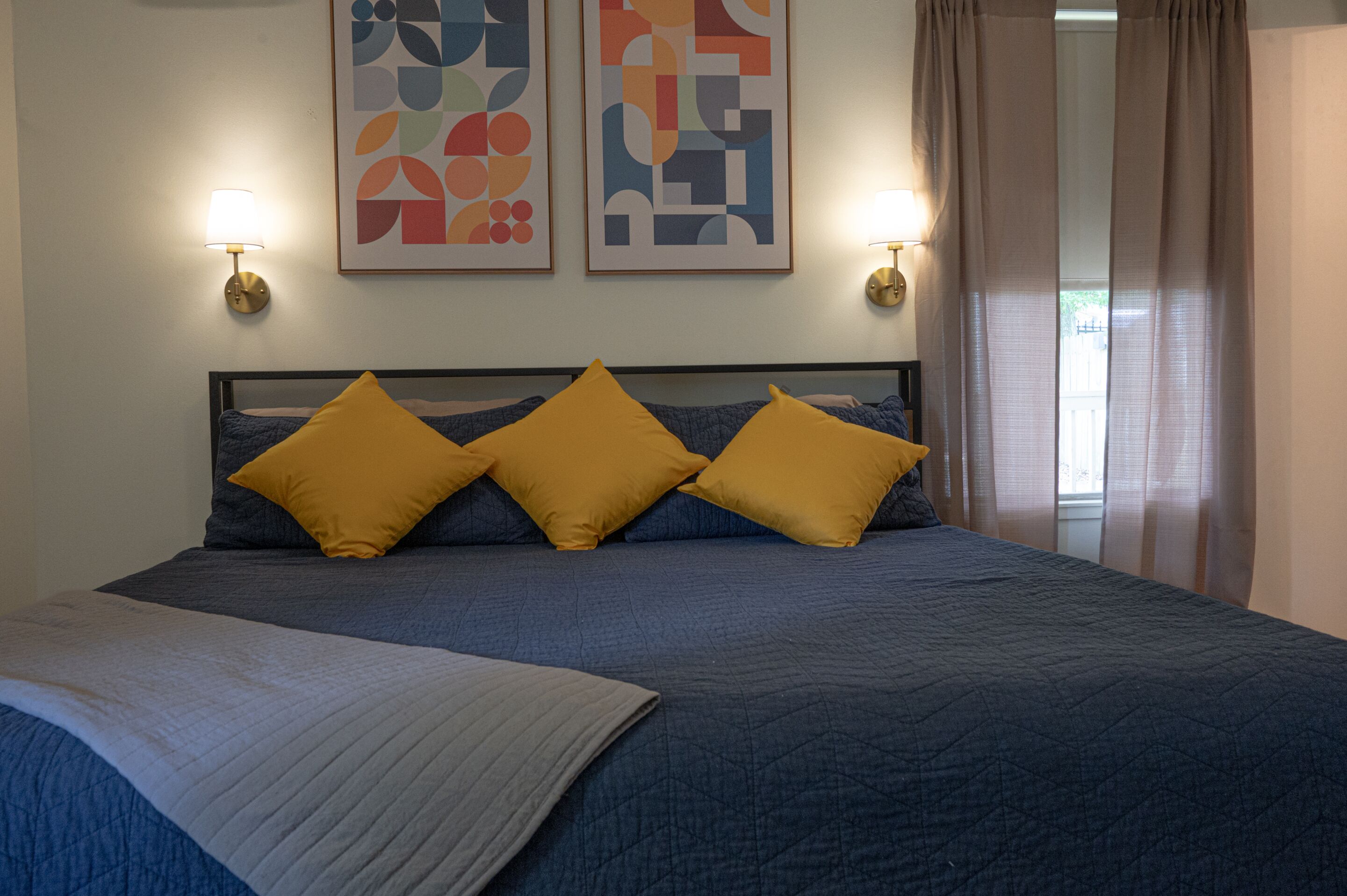 A bed with a blue quilt, three yellow pillows, and two wall-mounted lamps.