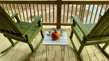 Une terrasse en bois avec deux fauteuils à bascule verts et une petite table sur laquelle se trouvent une citrouille et deux tasses.