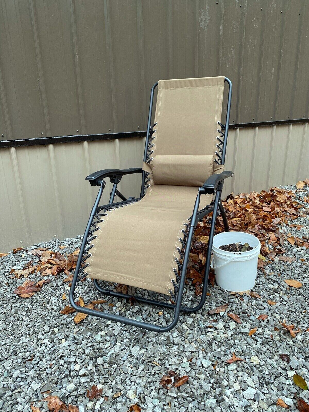 A reclining chair with a metal frame and beige fabric, positioned on gravel with a white bucket nearby.