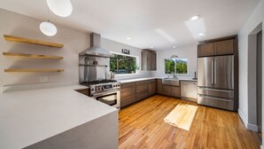 Una cocina moderna con suelo de madera, electrodomésticos de acero inoxidable y estanterías empotradas de madera.