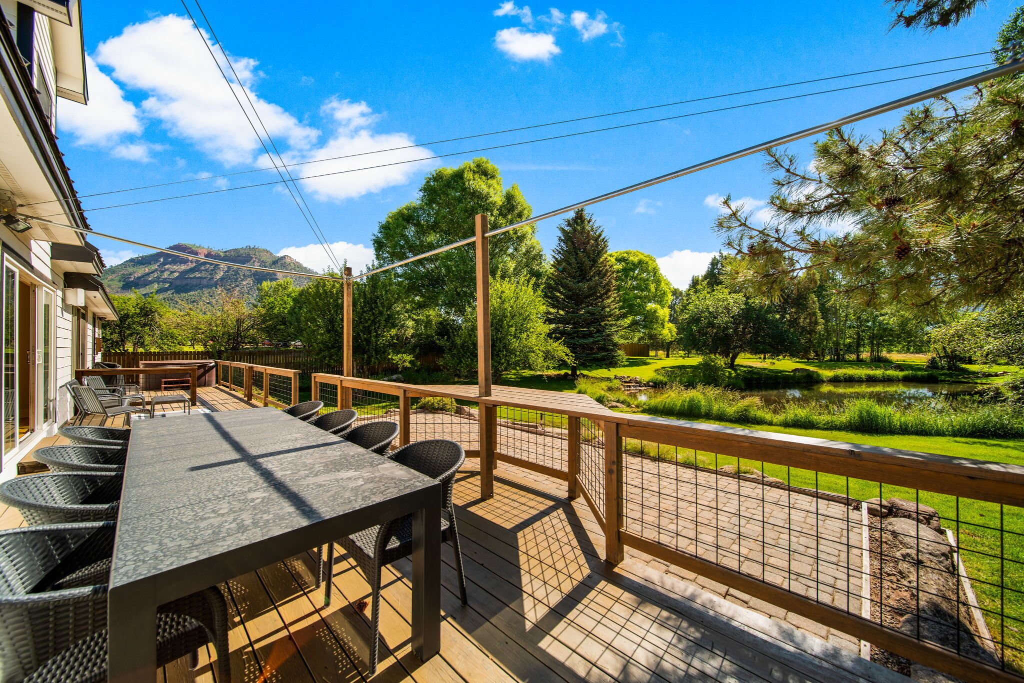 Une terrasse en bois avec une table et des chaises, donnant sur un jardin aménagé avec un étang et des arbres.