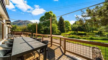 Une terrasse en bois avec une table et des chaises, donnant sur un jardin aménagé avec un étang et des arbres.