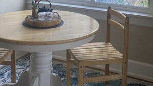 A round wooden table with a white pedestal base, two wooden chairs, and a window with a leaf-patterned view. - Cozy 1-bedroom apartment in lovely Alma with WiFi, AC (Alma)