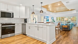 Eine moderne Küche mit weißen Schränken, einer eingebauten Mikrowelle und einem Backofen. Es gibt einen Essbereich mit einem blauen Sofa und einem Tisch.