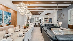 A modern dining area with a chandelier, wooden ceiling beams, and a large painting on the wall. - Fairway Tropic Oasis: Themed Bedrooms, Arcade, Basketball Court, Near Disney (Kissimmee)