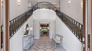 A spacious hallway with a staircase, a console table with a mirror, and a bench. - Fairway Tropic Oasis: Themed Bedrooms, Arcade, Basketball Court, Near Disney (Kissimmee)