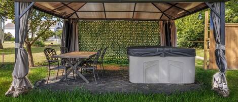 Een overdekt terras met een tafel, stoelen, een jacuzzi en een sierhekwerk.