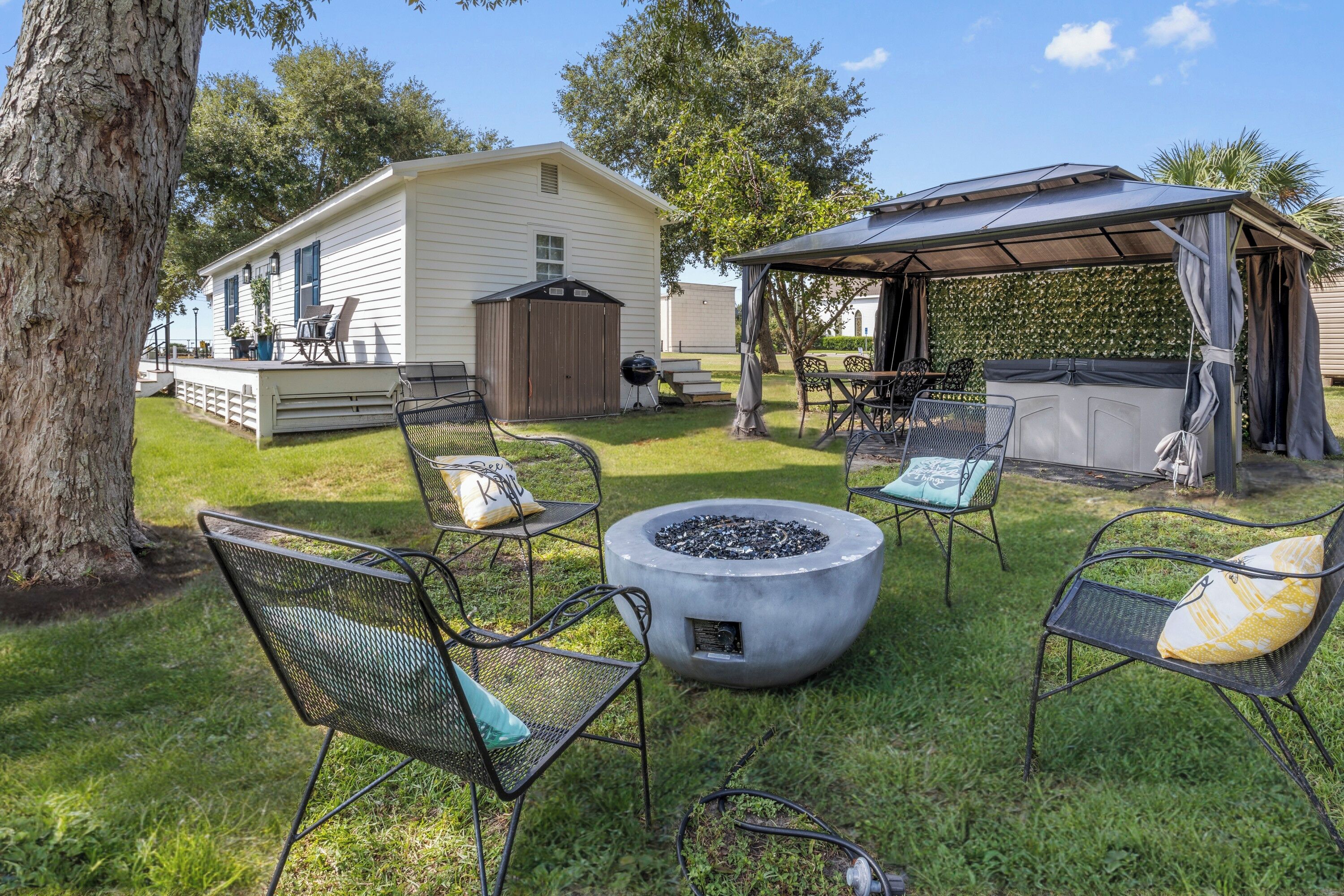Un jardin avec un espace salon couvert, un foyer extérieur et une maison mobile.