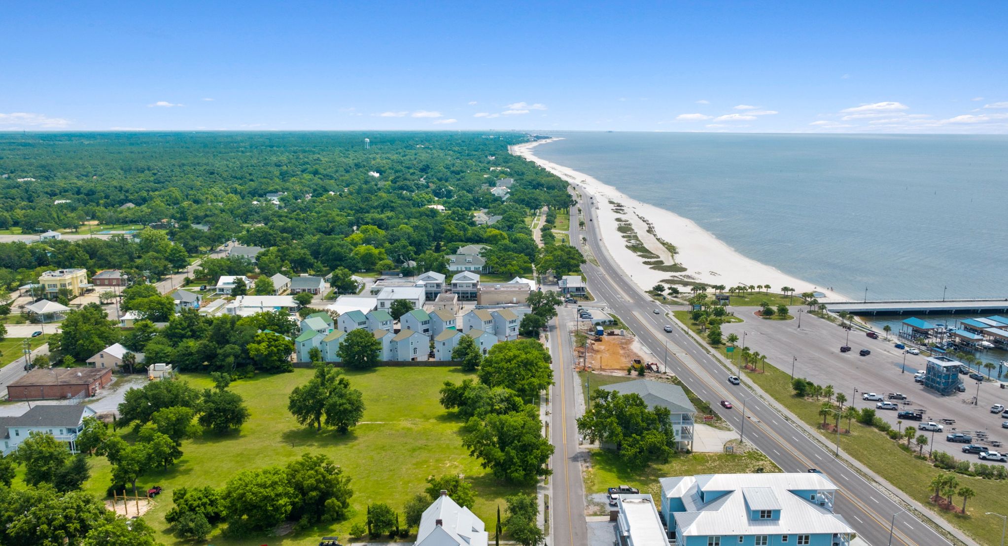 An aerial view of a coastal town with a beach, roads, and residential buildings.