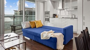 A modern living room with a blue sofa, a glass coffee table, and a balcony with a view of buildings. - Lovely Downtown Condo with Iconic CN Tower View! (Toronto)