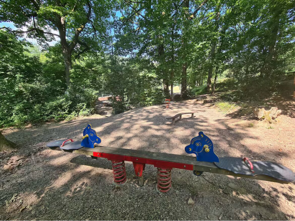 A seesaw with a wooden bench in a wooded area.