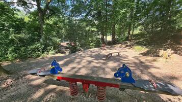 A seesaw with a wooden bench in a wooded area.