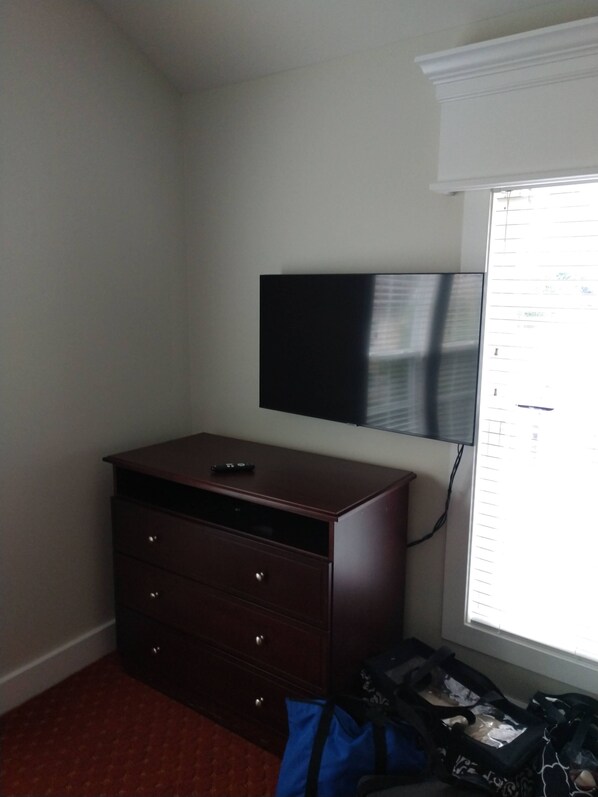 Een kamer met een donkere houten dressoir, een flatscreen televisie aan de wand en een raam met zonwering.
