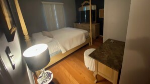 A bedroom with a bed, bedside table, lamp, dresser, and a window with curtains.