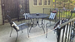 A patio with a round table and four chairs, a decorative gate, and a house with a window.