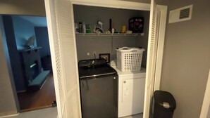A compact laundry area with a washer and dryer, a small shelf with toiletries, and a laundry basket.