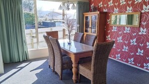 Un coin repas comprenant une table à plateau en verre, des chaises en osier, un meuble avec des portes en verre et une vue dégagée grâce à de grandes fenêtres.