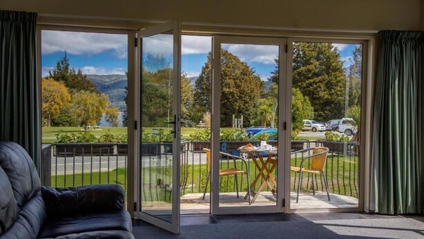 Une pièce dotée d’une porte-fenêtre coulissante donnant sur un balcon avec vue sur un lac, des arbres et des voitures.