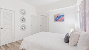 A bedroom with a large bed, white walls, and three doors. - Leisure Loft Refreshed By the Ocean (San Juan)