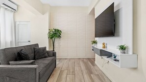 A modern living room with a grey sofa, a mounted TV, and a white shelf with decorative items. - Leisure Loft Refreshed By the Ocean (San Juan)