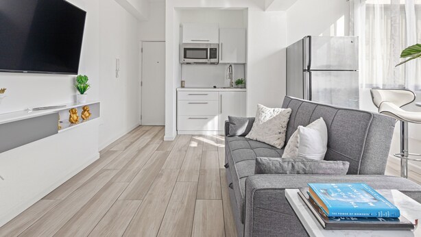 A modern living room with a grey sofa, a flat-screen TV, and a bookshelf. - Leisure Loft Refreshed By the Ocean (San Juan)