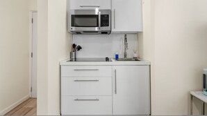 A compact kitchen with white cabinets, a stainless steel microwave, and a sink. - Leisure Loft Refreshed By the Ocean (San Juan)