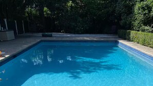 Een rechthoekig zwembad met helderblauw water, omgeven door een terras met een kiezelstructuur.