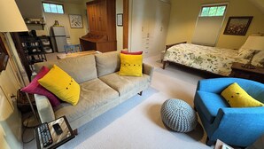 Een ruime woonkamer met een bank, fauteuil en een bed met een bloemenprint.