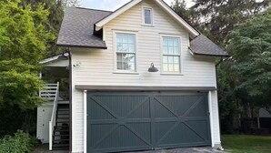 Een twee verdiepingen tellend huis met een donkergroene garage deur, een klein raam op de bovenverdieping en een trap naar een overdekte veranda.