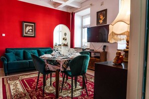 Un coin repas avec un mur rouge, un canapé turquoise, une table dressée pour quatre personnes et un téléviseur en arrière-plan.