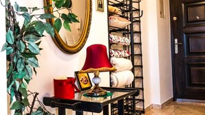 A hallway with a large mirror, a red lamp, a small table with a picture frame, a plant, and a coat rack with folded items. - Górna Royal Red Apartment (Lublin)