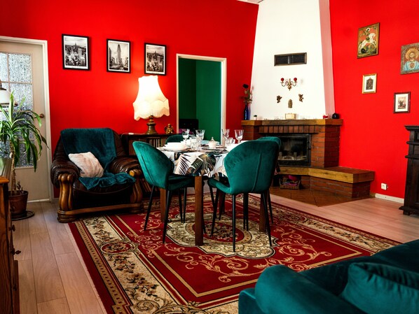 Une salle à manger avec un mur rouge, une porte verte et une cheminée. On y trouve trois chaises et une table mise pour le repas.