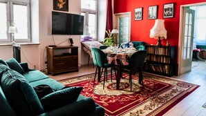 A living room with a red wall, a green sofa, a dining table with chairs, a TV, and a bookshelf. - Górna Royal Red Apartment (Lublin)