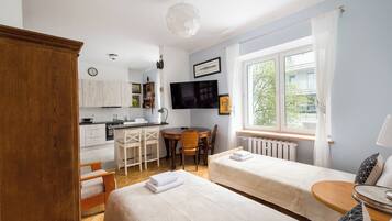 Hotellihuone, jossa on kaksi sänkyä, ruokailutila, keittiö ja suuri ikkuna.