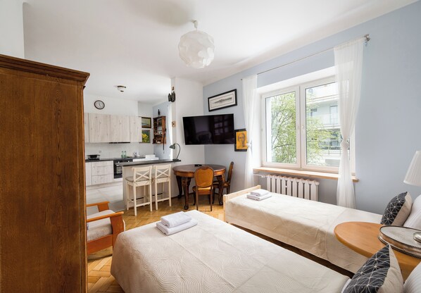 A hotel room with two beds, a dining area, a kitchen, and a large window.
