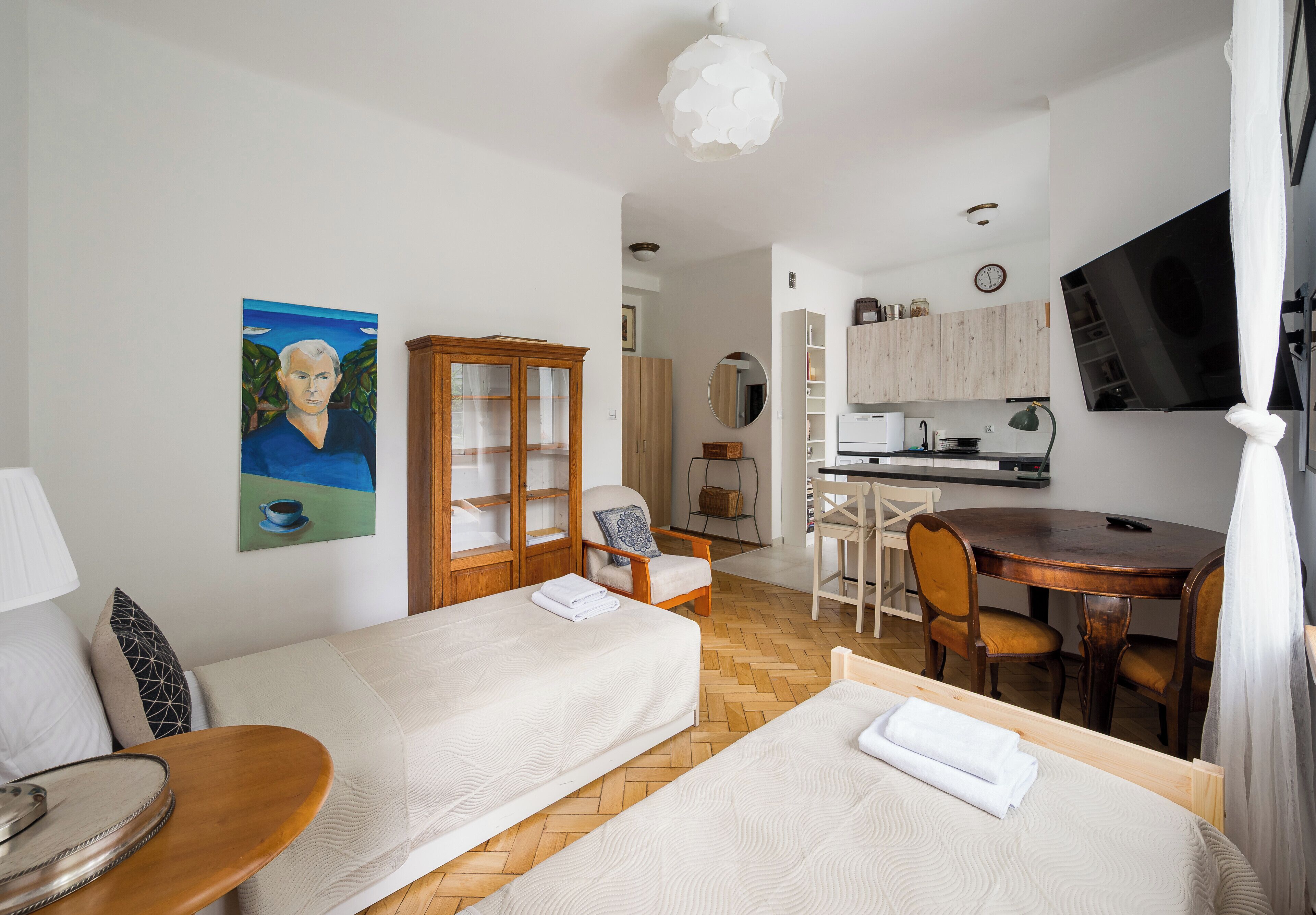 Hotellihuone, jossa on kaksi sänkyä, ruokapöytä, keittiö sekä televisio.