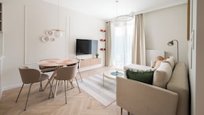 A modern living room with a sofa, a dining table with chairs, a TV, and a large window with curtains. - Malinova Leaf Apartment (Warszawa)